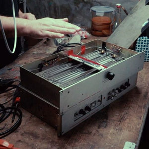 Hands opening a Fairchild spring reverb unit on a workshop bench, internal spring and circuit components