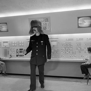Vintage mid-century broadcast control room, person in a fur ushanka hat, rows of control panels, black