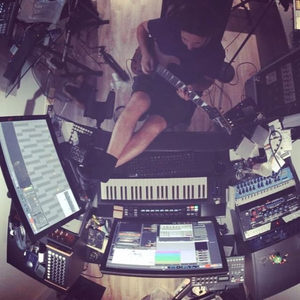 Top-down fisheye of a producer playing guitar in the studio, surrounded by synthesizers and screens