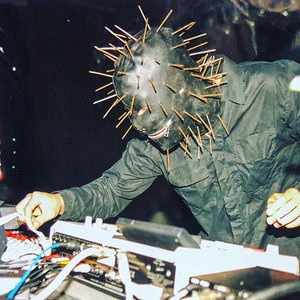 Performer in a spiked metal nail mask operating stage equipment under dramatic stage lighting