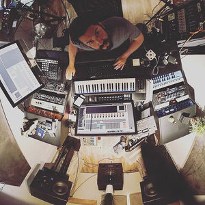 Top-down fisheye view of a producer working at a keyboard-equipped studio desk with synthesizers around