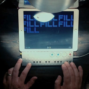 Hands programming a small MIDI controller below an iPad showing a fill pattern in a Zombie Nation session