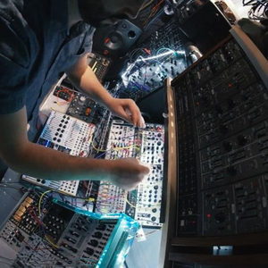 Overhead fisheye view of a producer patching a large modular synthesizer, bathed in teal studio light