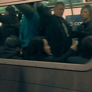 Passengers seen through a crowded subway carriage window, shot from outside the moving train in low light