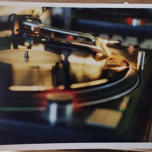 Lomography close-up of a Technics SL-1210 turntable tonearm resting on a spinning vinyl record, warm