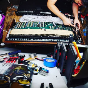 A vintage polyphonic synthesizer open on a workshop bench with circuit boards exposed and tools scattered