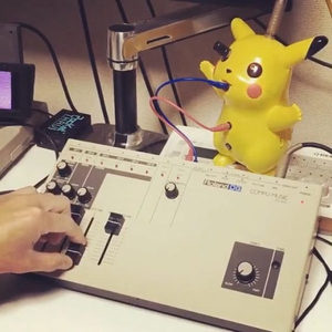 Roland DG Compu Music and Pikachu toy on a studio desk, colorful patch cables and MIDI adapter visible