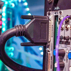 DB25 connector plugged into a Zombie Nation patchbay with blue and purple patch cables, teal stage lighting