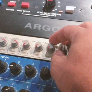 Hand adjusting knobs on a Doepfer MS-404 bass synthesizer in a rack below an Argosy Space Station delay