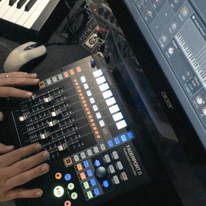 Hands operating a Presonus FaderPort 8 controller with Bitwig Studio sampler open on a monitor, keyboard