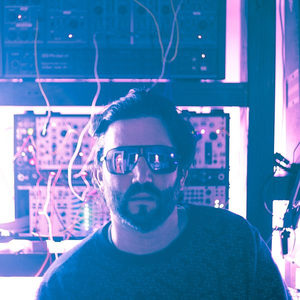 Florian Senfter in purple neon light with dark sunglasses, modular synthesizer rack visible behind him