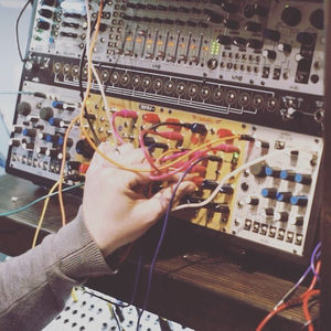 Hand reaching toward a Zombie Nation Eurorack modular synthesizer with patch cables, dark studio atmosphere