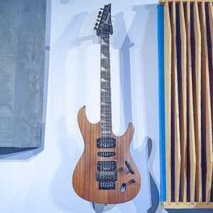 Ibanez S-series electric guitar in natural finish hanging on a white studio wall, acoustic panel to the
