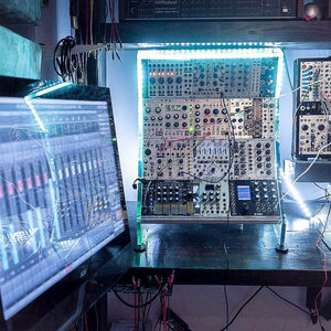 Zombie Nation studio modular synthesizer rack lit by LED strip alongside a large monitor showing a DAW