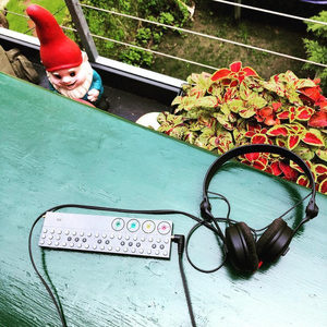 Teenage Engineering OP-Z and headphones on an outdoor turquoise table, garden gnome and potted plants