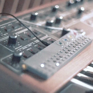 Sequential Prophet-5 synthesizer panel alongside a Teenage Engineering OP-Z on a wooden desk, dreamy soft