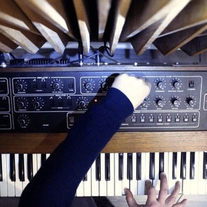 Top-down view of a Sequential Circuits Prophet-5 synthesizer, hands on the keys and filter section controls