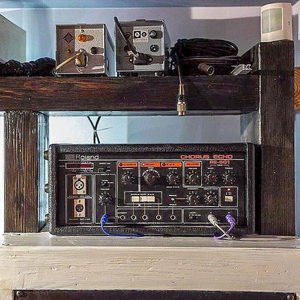 Roland RE-201 Space Echo on a wooden studio shelf with vintage outboard gear stored on the rack above it