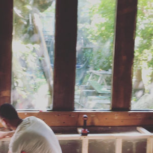 Studio workspace under construction, wooden desk frame near garden windows, person assembling with clamps