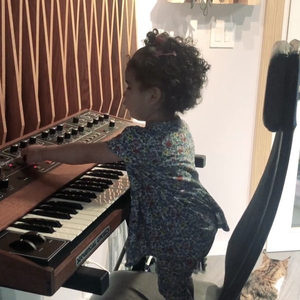 Toddler sitting at a keyboard in the Zombie Nation studio, seen from the side, warm lighting