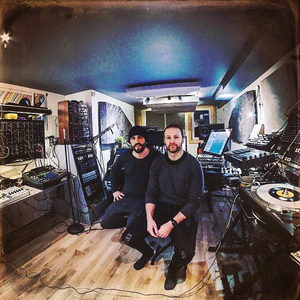 Two producers sitting in the Zombie Nation studio surrounded by synthesizers and turntables, fisheye wide