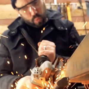 Person in safety glasses using an angle grinder on metal, bright sparks flying in a workshop setting