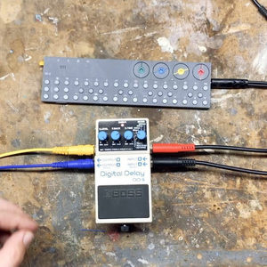 Boss Digital Delay pedal alongside a small Eurorack palette case on concrete, colorful cables behind