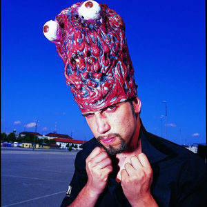 Florian Senfter circa 2000 in a latex brain headpiece with googly eyes, fists raised, car park behind