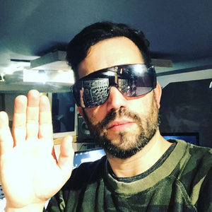 Florian Senfter studio selfie in large mirrored sunglasses, modular rack reflected in lenses, hand raised