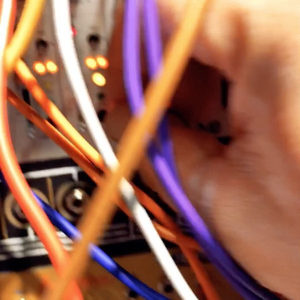 Extreme close-up of a hand patching a Eurorack module with orange, purple and blue cables in soft focus