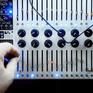 KOMA Komplex Sequencer panel with blue step buttons, hand patching a cable in, Zombie Nation studio