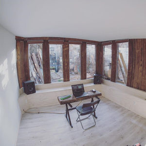 Fisheye view of a minimal workspace with six large windows, small desk with laptop and two studio monitors