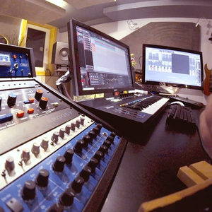 Studio desk with a mixing console, multiple faders and dual monitors showing DAW and plugin sessions