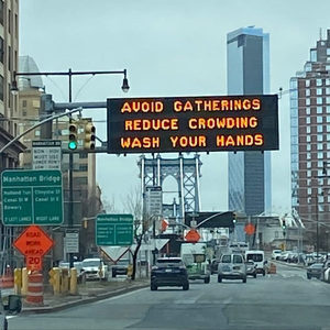 LED highway sign reading Avoid Gatherings Reduce Crowding Wash Your Hands, Manhattan Bridge behind