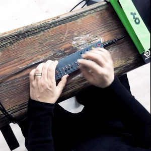 Person at an outdoor table using a small keyboard controller in a folded hardcase, hands in motion