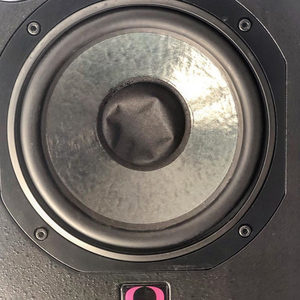 Close-up of a Quested studio monitor woofer cone with the pink Quested logo badge visible at the bottom