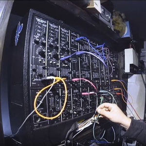 Person patching a Roland System 700 modular synthesizer, fisheye side view with coloured patch cables