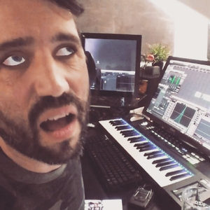 Selfie with a white-eye filter in the studio, DAW open on two monitors and a MIDI keyboard behind
