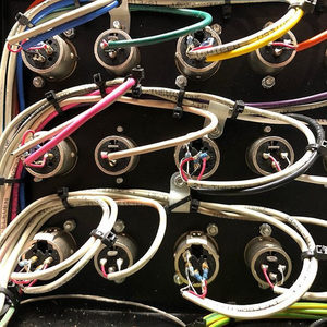 Close-up of XLR connectors and colorful cables plugged into a studio patchbay, black panel background
