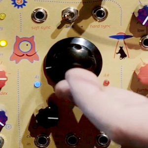 Hand adjusting a large knob on a yellow Eurorack module with soft sync and hard sync labelling visible